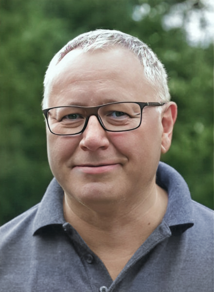 Ein Profilbild von Dr. Oelmann, der eine Brille trägt, ein graublaues Oberteil und graue, kurze Haare.